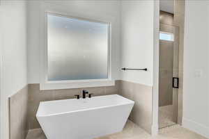 Bathroom with a freestanding bath, tile walls, a shower stall, and a wainscoted wall