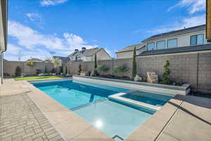 View of swimming pool featuring a pool with connected hot tub, a fenced backyard, and a patio area