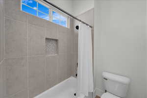 Bathroom featuring toilet and shower / bathtub combination with curtain