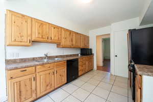 Kitchen featuring black appliances, light tile patterned flooring, and light brown cabinetry