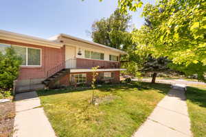 View of front of house featuring brick siding, a front yard, and stairs