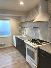 Kitchen featuring white appliances, custom exhaust hood, open shelves, light wood-style flooring, and dark cabinetry