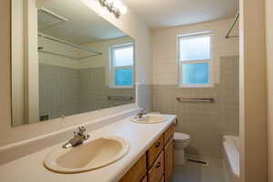 Bathroom with double vanity, tile walls, shower / bath combination, and light tile patterned floors