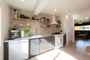 Kitchen with white appliances, light countertops, wall chimney range hood, open shelves, and beam ceiling