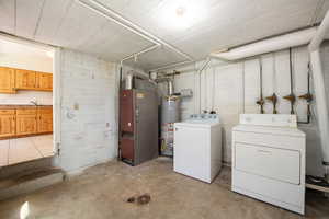 Laundry area featuring unfinished concrete floors, heating unit, strapped water heater, and washer and dryer