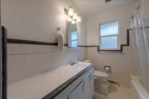 Full bathroom with tile walls, vanity, light tile patterned floors, and shower / bath combo