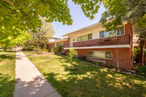 View of front facade with brick siding, a front yard, and a balcony