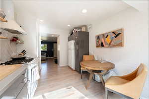 Kitchen with white appliances, custom exhaust hood, recessed lighting, light wood-type flooring, and open shelves