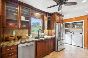 Kitchen featuring appliances with stainless steel finishes, washing machine and dryer, decorative backsplash, glass insert cabinets, and a ceiling fan