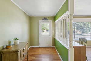 Doorway with ornamental molding, a textured ceiling, and wood finished floors