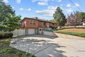 View of front of property with a gate, a garage, driveway, brick siding, and a chimney