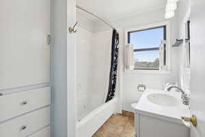 Bathroom featuring vanity, shower / bathtub combination with curtain, ornamental molding, and tile patterned flooring