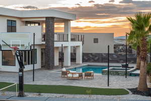 Back of house at dusk featuring a patio, a pool with connected hot tub, and stucco siding