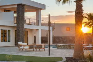 Back of property at dusk featuring a patio area, stucco siding, a pool with connected hot tub, and a balcony