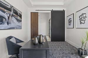 Carpeted home office with a barn door and a tray ceiling