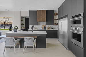 Kitchen with appliances with stainless steel finishes, open shelves, modern cabinets, dark cabinetry, and a textured ceiling