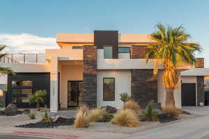 Contemporary home with stone siding, stucco siding, a balcony, and an attached garage