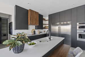 Kitchen featuring open shelves, modern cabinets, appliances with stainless steel finishes, and dark cabinetry