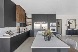 Kitchen featuring modern cabinets, dark cabinets, open shelves, light countertops, and tasteful backsplash