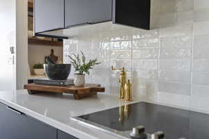 Kitchen view of black electric stovetop, backsplash, and light countertops