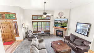 Living room with a tiled fireplace, ceiling fan, and wood finished floors