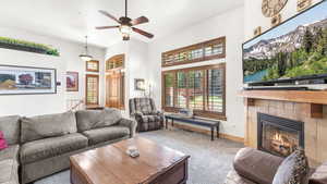 Living area featuring carpet flooring, a tiled fireplace, a ceiling fan, and a towering ceiling