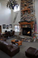 Carpeted living area with a towering ceiling, a chandelier, an office area, and a stone fireplace