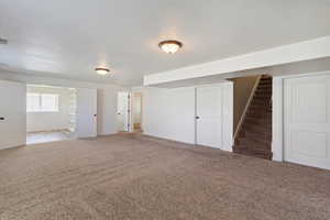 Basement featuring light colored carpet, stairway, and a textured ceiling