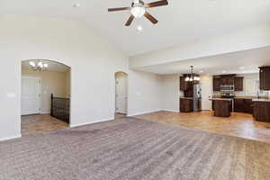 Unfurnished living room featuring light carpet, a chandelier, arched walkways, a ceiling fan, and high vaulted ceiling