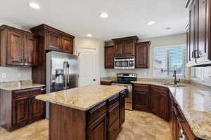 Kitchen featuring appliances with stainless steel finishes, recessed lighting, a center island, dark brown cabinetry, and light stone countertops