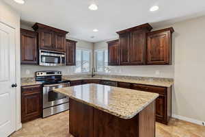 Kitchen featuring appliances with stainless steel finishes, dark brown cabinets, light stone countertops, recessed lighting, and a textured ceiling