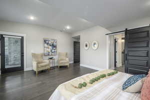 Bedroom with a barn door, vaulted ceiling, access to exterior, dark wood-type flooring, and recessed lighting