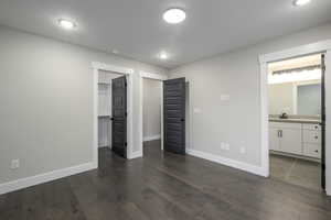 Unfurnished bedroom featuring dark wood-style flooring, a spacious closet, ensuite bathroom, and recessed lighting