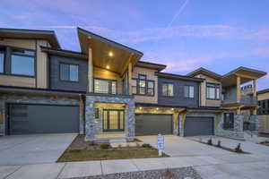 Contemporary house with a balcony, stone siding, concrete driveway, and an attached garage