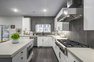 Kitchen featuring wall chimney exhaust hood, appliances with stainless steel finishes, dark wood finished floors, white cabinets, and recessed lighting