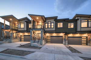 Contemporary home with a balcony, driveway, an attached garage, and stone siding