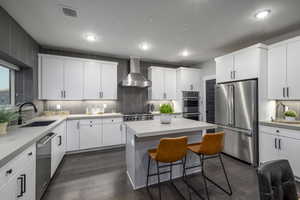 Kitchen with appliances with stainless steel finishes, decorative backsplash, a breakfast bar, wall chimney range hood, and white cabinets