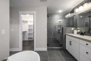 Full bath featuring dark tile patterned flooring, vanity, a spacious closet, a freestanding tub, and a stall shower