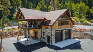 View of front of house with stone siding, a standing seam roof, an attached garage, a forest view, and a patio
