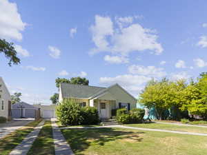 Bungalow-style home with a detached garage, a front lawn, and a shingled roof