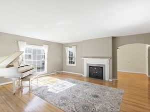 Living room featuring arched walkways, healthy amount of natural light, wood finished floors, and a fireplace with flush hearth