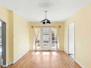 Unfurnished dining area featuring arched walkways, french doors, and light wood-style floors