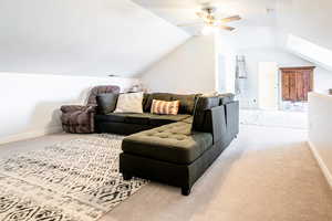 Carpeted living area with vaulted ceiling, a ceiling fan, and a skylight