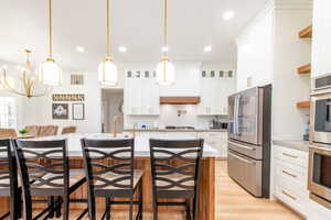 Kitchen with stainless steel appliances, light wood-style flooring, a kitchen breakfast bar, white cabinetry, and recessed lighting