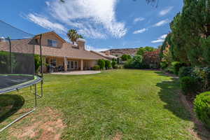 View of grassy yard featuring a trampoline, french doors, and a patio area