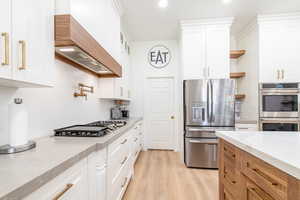Kitchen featuring stainless steel appliances, custom exhaust hood, open shelves, light wood finished floors, and white cabinets