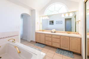 Bathroom with vaulted ceiling, double vanity, a bath, and tile patterned flooring