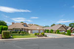 View of front of house featuring an attached garage, concrete driveway, a chimney, a front lawn, and brick siding