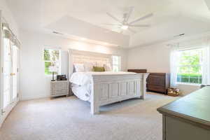 Bedroom with a raised ceiling, multiple windows, and light carpet