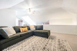 Living area featuring vaulted ceiling, ceiling fan, a textured ceiling, light colored carpet, and a skylight